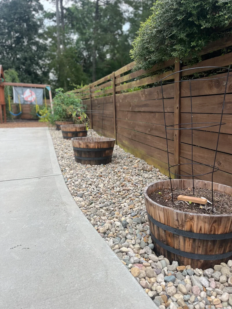 River rock border and planter barrels along a wood fence